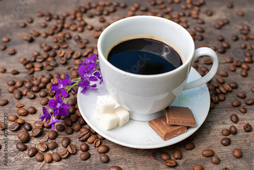 white cup of coffee on a wooden table  chocolate  sugar and coffee beans 