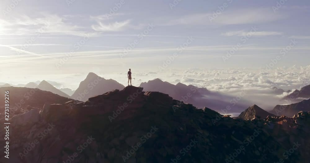 Aerial trail runner man standing on mountain top peak goal looking horizon view.drone shot.Wild nature outdoors at sunrise or sunset backlit.Training activity,sport,effort,challenge,willpower concepts