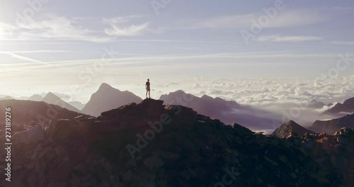 Aerial trail runner man standing on mountain top peak goal looking horizon view.drone shot.Wild nature outdoors at sunrise or sunset backlit.Training activity,sport,effort,challenge,willpower concepts