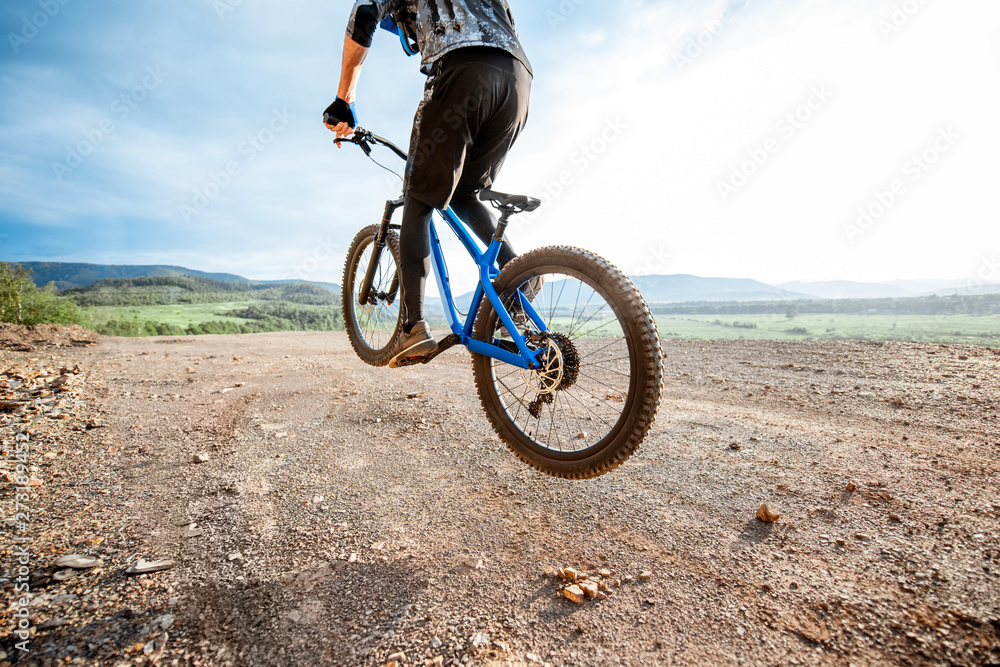 Fototapeta premium Professional well-equipped cyclist riding bicycle on the rocky mountains with beautiful landscape view during the sunset