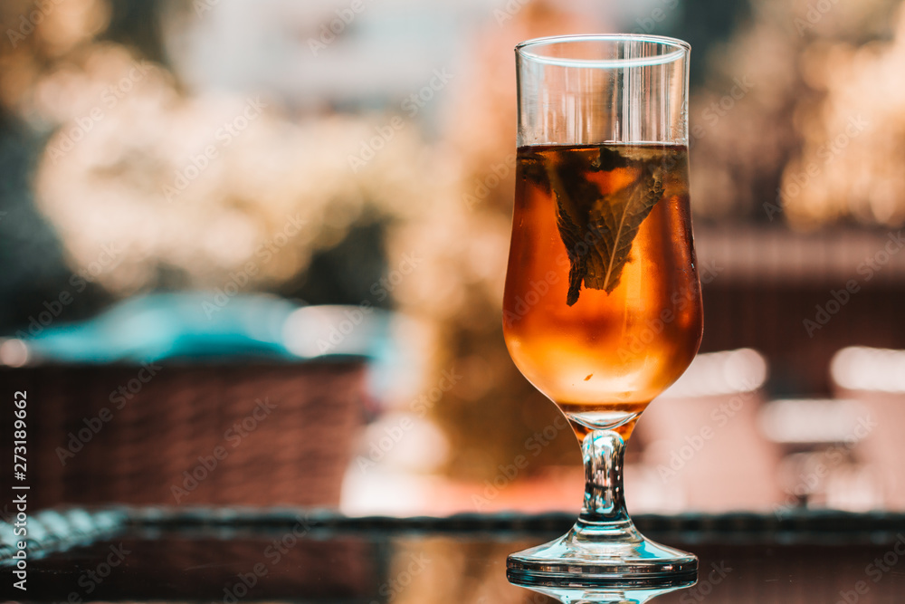 Elegant glass filed with brown fruity juice and mint leaves sitting on a table at a bar or restaurant – Natural and healthy sweet drink consumed on hot summer days Elegant glass filed with brown fruity juice and mint leaves sitting on a table at a bar or restaurant – Natural and healthy sweet drink consumed on hot summer days