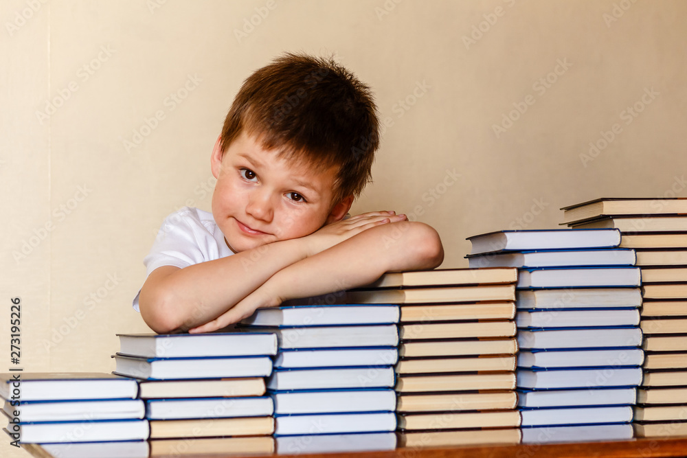smiling six-year-old boy sitting at the table with his hands on books smiling six-year-old boy sitting at the table with his hands on books