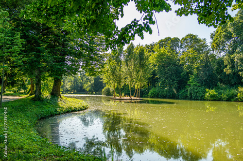 View of an Italian summer park with old trees and a pond