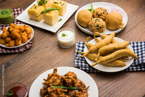 Indian Tea time snacks  in group includes Veg Samosa, Kachori/kachaudi, aloo bonda, khaman dhokla, bread, onion,chilli and moong pakora/pakoda/bhaji/bhajji/Bhajiya/bajji with sauces, selective focus photo