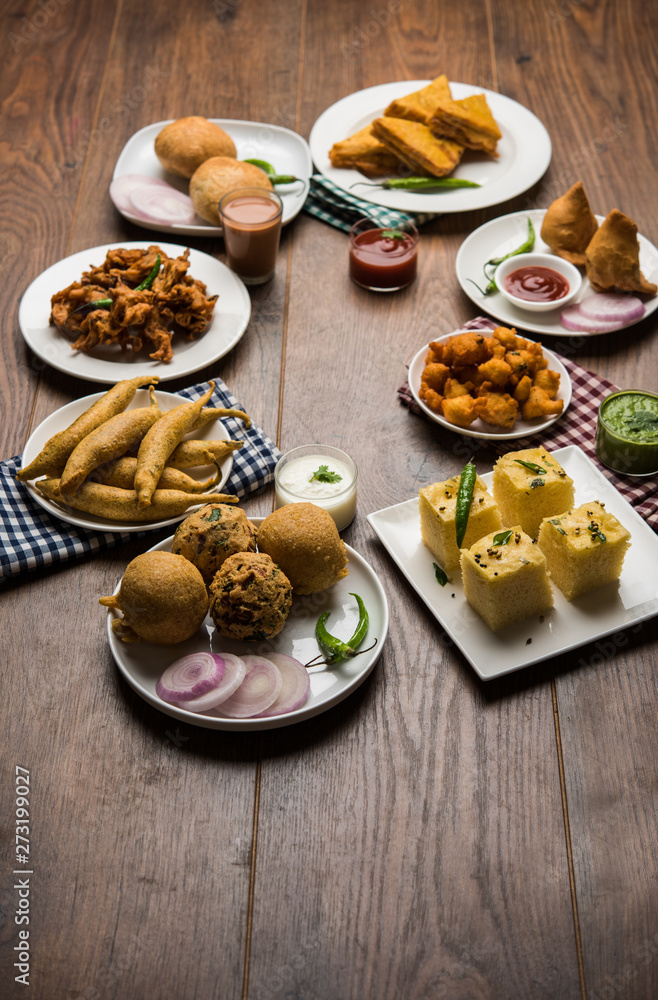 Indian Tea time snacks  in group includes Veg Samosa, Kachori/kachaudi, aloo bonda, khaman dhokla, bread, onion,chilli and moong pakora/pakoda/bhaji/bhajji/Bhajiya/bajji with sauces, selective focus