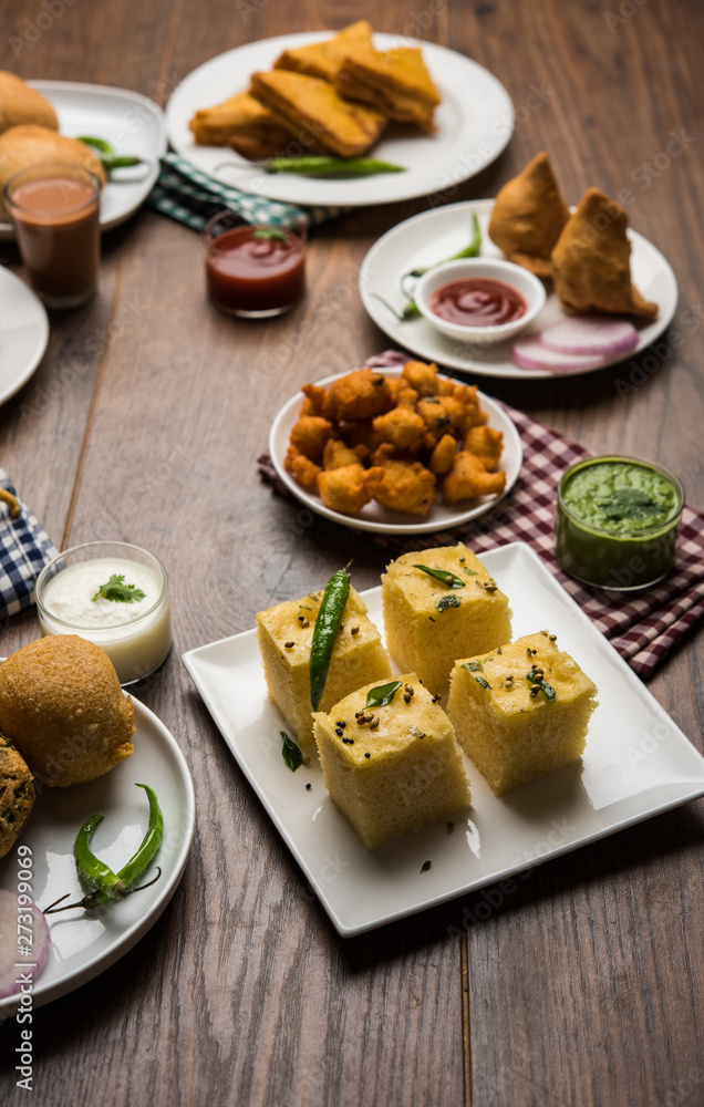 Indian Tea time snacks  in group includes Veg Samosa, Kachori/kachaudi, aloo bonda, khaman dhokla, bread, onion,chilli and moong pakora/pakoda/bhaji/bhajji/Bhajiya/bajji with sauces, selective focus