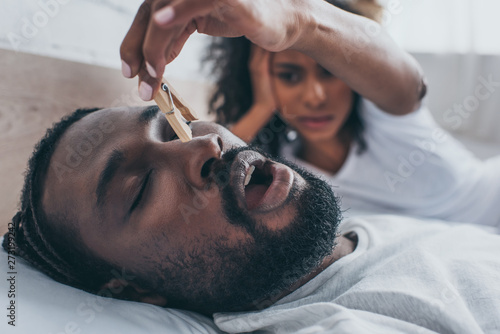 Photography selective focus of snoring african american man near wife holding wooden pin