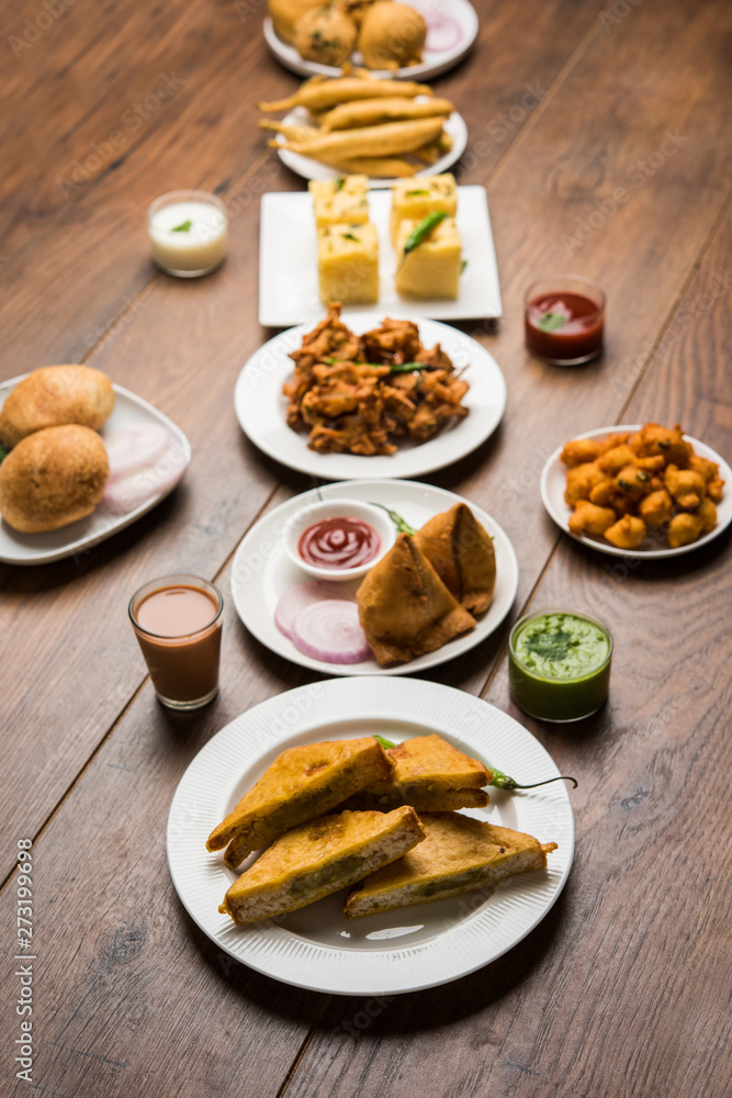 Indian Tea time snacks in group includes Veg Samosa, Kachori/kachaudi, aloo bonda, khaman dhokla, bread, onion,chilli and moong pakora/pakoda/bhaji/bhajji/Bhajiya/bajji with sauces, selective focus Indian Tea time snacks in group includes Veg Samosa, Kachori/kachaudi, aloo bonda, khaman dhokla, bread, onion,chilli and moong pakora/pakoda/bhaji/bhajji/Bhajiya/bajji with sauces, selective focus