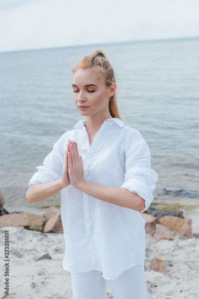 attractive young woman with closed eyes and praying hands near sea attractive young woman with closed eyes and praying hands near sea