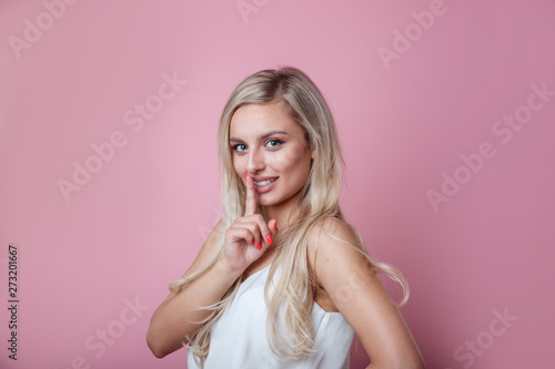 Pretty young female with cheerful expression, tells her secret to close friend, makes silence sign