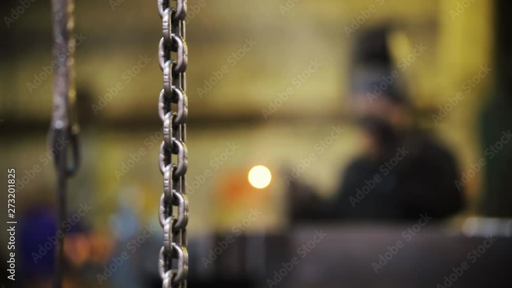The chain hangs from the ceiling - a welder works at the plant