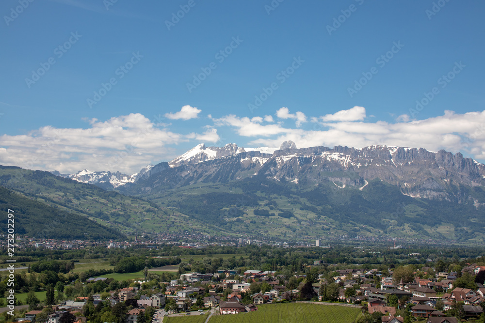 Panorama of an alpine landscape with high mountains, green meadows and trees in spring with snow in Swiss Alps-Switzerland Panorama of an alpine landscape with high mountains, green meadows and trees in spring with snow in Swiss Alps-Switzerland