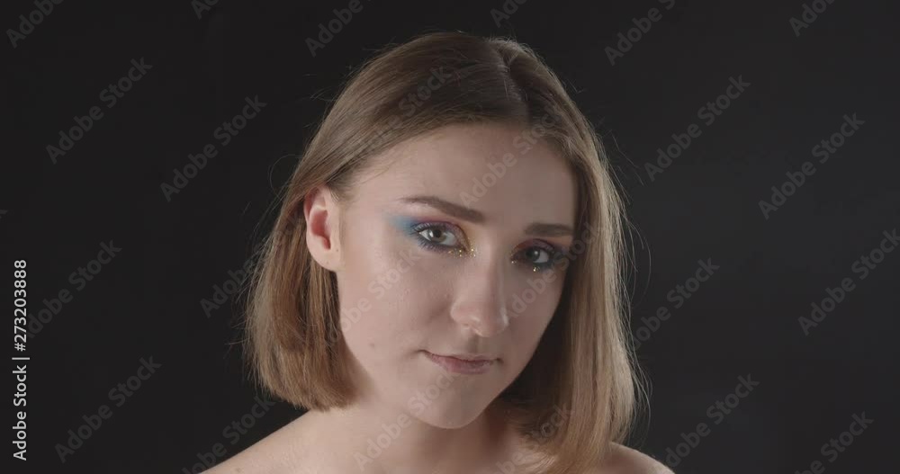 Closeup shoot of young pretty caucasian short haired female with cute glitter makeup raising her eyebrows looking at camera with background isolated on black Closeup shoot of young pretty caucasian short haired female with cute glitter makeup raising her eyebrows looking at camera with background isolated on black