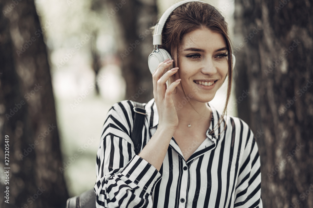 Outdoor Summer Portrait of Young Beautiful Girl in White Striped Stylish Dress Listens Music in Headphones Outdoor Summer Portrait of Young Beautiful Girl in White Striped Stylish Dress Listens Music in Headphones