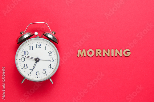 Retro alarm clock on red background with text morning with letters.
