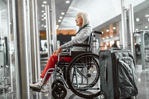 Smiling mature lady on disabled carriage looking forward at airport