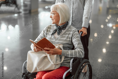 Female worker of airport moving elderly woman in wheelchair at hall