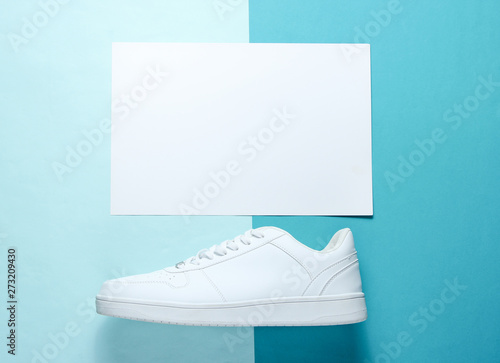 White sneaker on a blue background with a white sheet of paper for copy space, top view