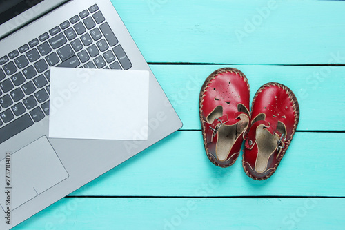 Father's day concept. Laptop with white piece of paper for copy space and kids sandals on wooden background, top view.