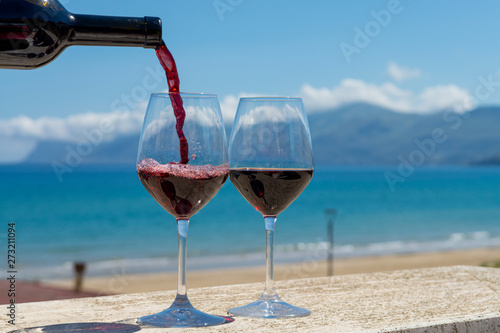 Canvas Print Waiter pouring red wine in wine glasses on outdoor terrace witn blue sea and mou