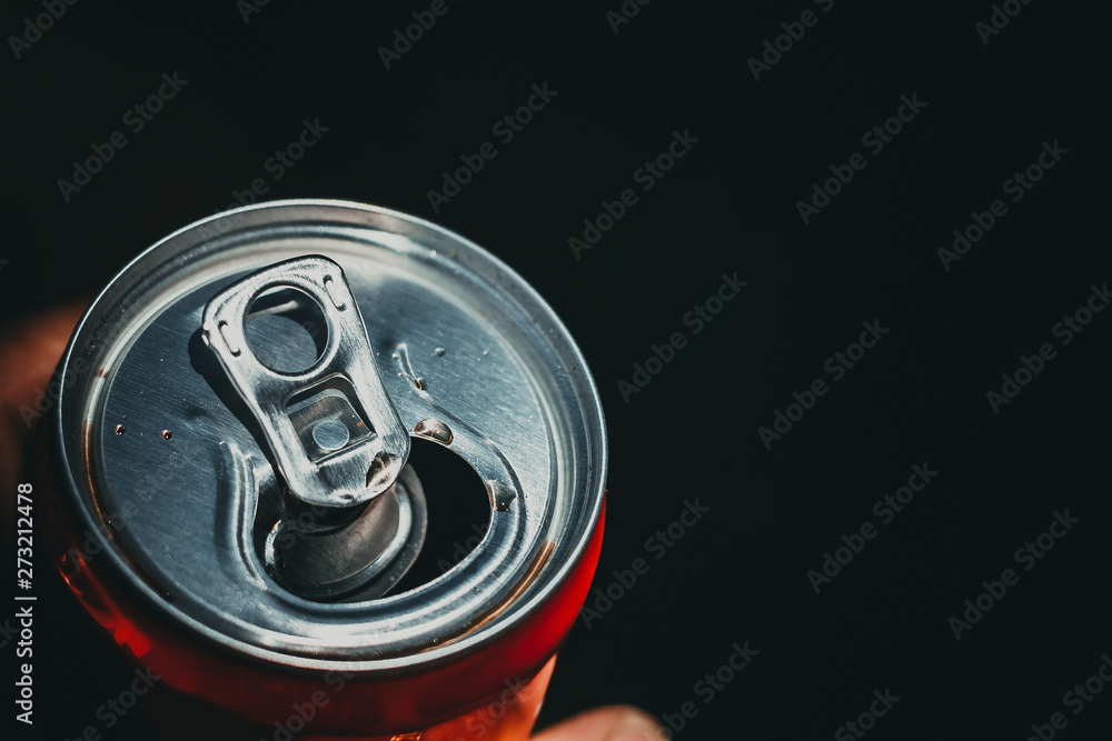 lighted tin open can with a soft drink in his hand on a dark background; there is a lot of copy space for text