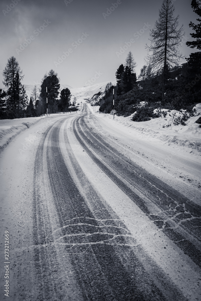 Obraz premium empty snowcapped road with car tracks in dramatic black and white foggy landscape mountain range in dolomites in wintertime, giau pass, italy