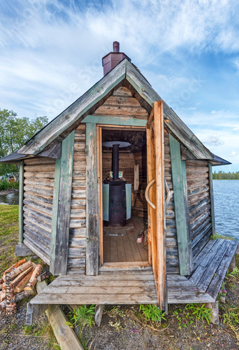 Swedish wooden sauna with open door, the woodstove is seen in interieur, the water of Gaxsjon lake is at background. Jamtland county in Northern Sweden. photo