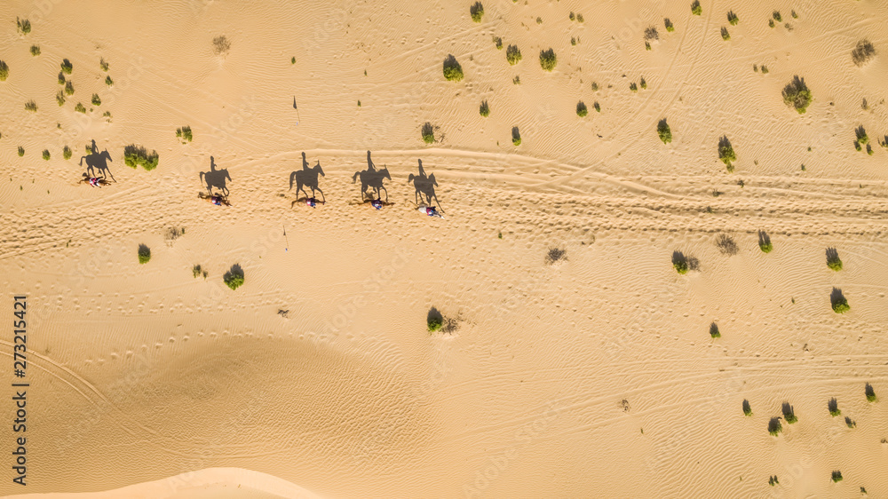Aerial view of people riding camels in the desert of Al Khatim in Abu Dhabi, U.A.E. Aerial view of people riding camels in the desert of Al Khatim in Abu Dhabi, U.A.E.
