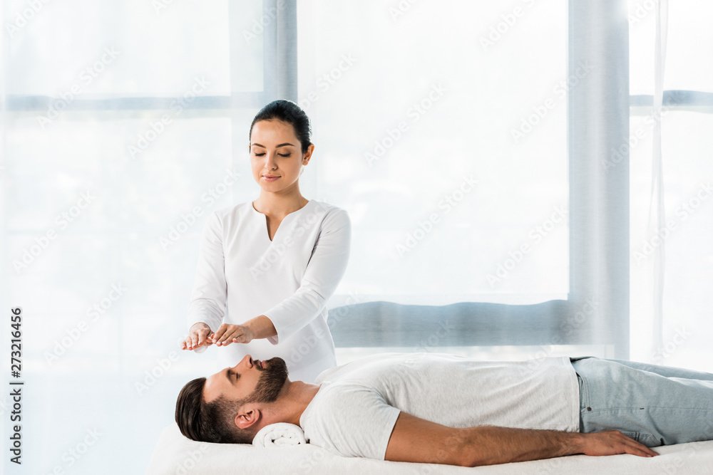 attractive healer putting hands above head while healing handsome bearded man attractive healer putting hands above head while healing handsome bearded man