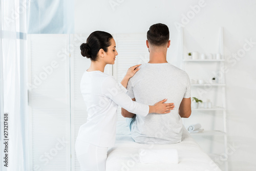 back view of man sitting on massage table near brunette healer © LIGHTFIELD STUDIOS