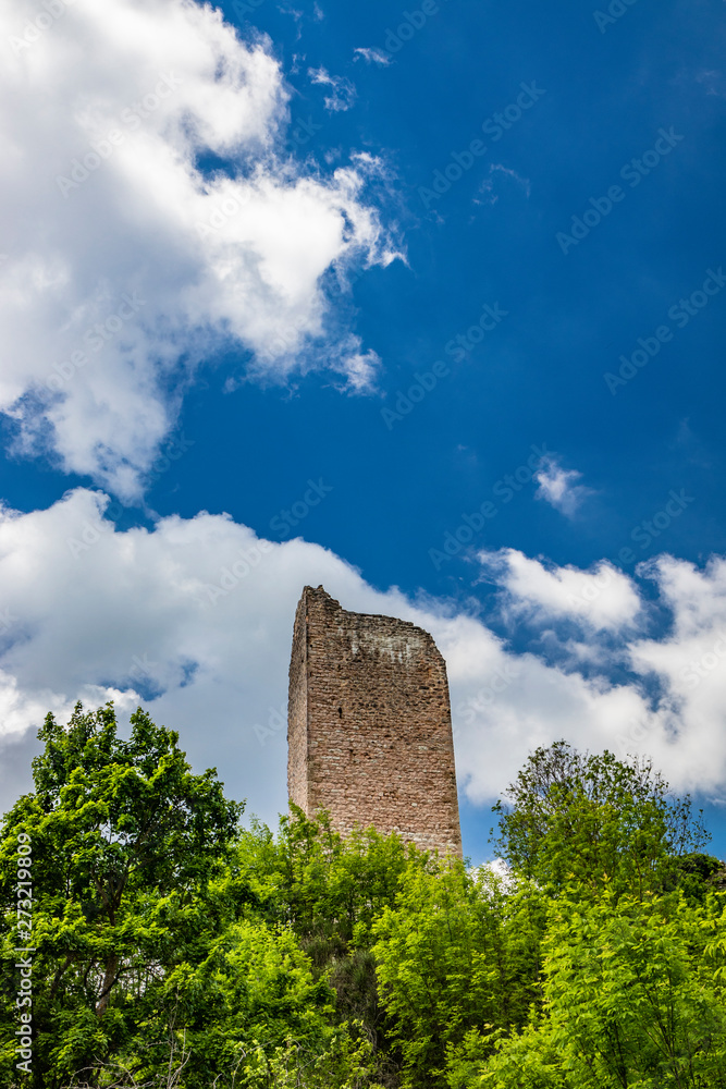 The ruin of the keep of the Trinci castle in Rasiglia. The remains of the tower, covered by vegetation, now collapsed and almost completely destroyed. The blue sky with clouds. Foligno, Umbria, Italy The ruin of the keep of the Trinci castle in Rasiglia. The remains of the tower, covered by vegetation, now collapsed and almost completely destroyed. The blue sky with clouds. Foligno, Umbria, Italy