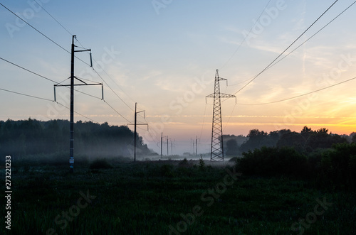 Power transmission line supporting structure at sunrise in the fog. Fields and power lines near Bryansk, Central Russia