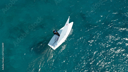 Aerial photo of small sail boat operated by children in exotic tropical bay with turquoise sea