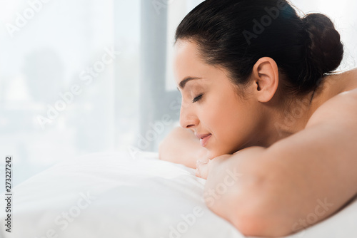 naked and cheerful girl with closed eyes lying on massage table