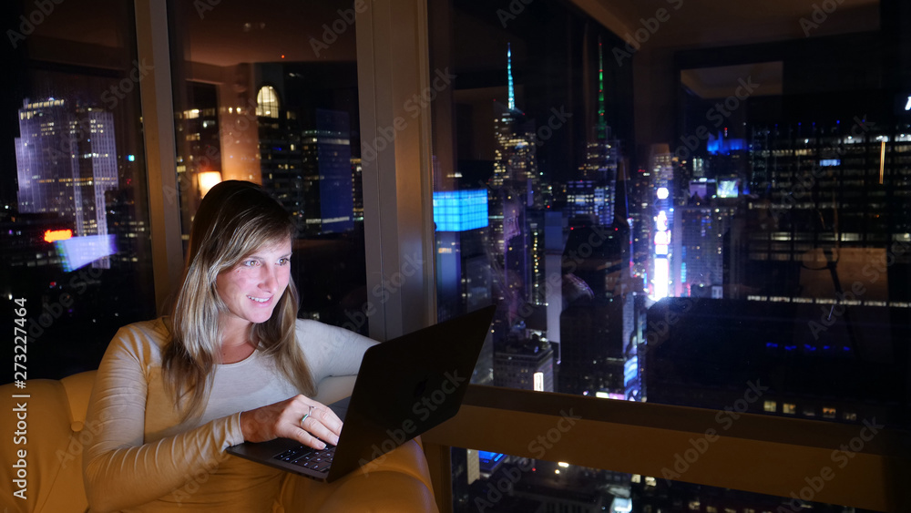 CLOSE UP: Cheerful woman sitting on the couch at night and working on her laptop CLOSE UP: Cheerful woman sitting on the couch at night and working on her laptop