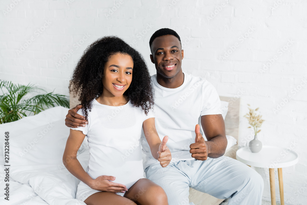 african american couple sitting on bed and gesturing thumbs up african american couple sitting on bed and gesturing thumbs up