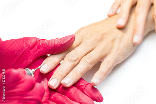 The manicurist in red silicone gloves processes nails of the woman of the client in beauty shop. The master removes a cuticle by method of hardware manicure
