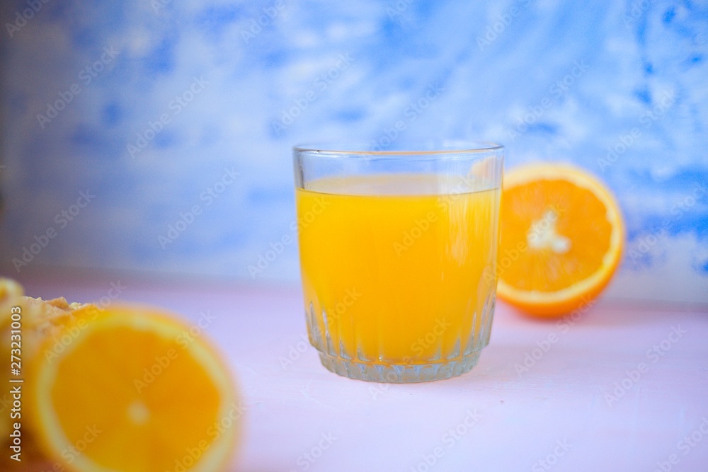 orange juice in glass with orange half on blue painted background orange juice in glass with orange half on blue painted background