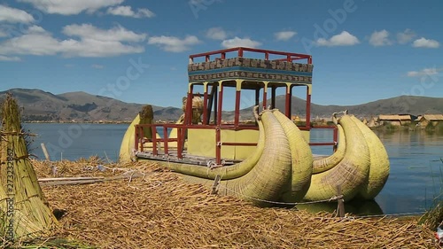 Close-up low angle still shot of Uros traditional coloured boat for carrying tourists and a stack of harvested totora reeds, Uros Island, Peru