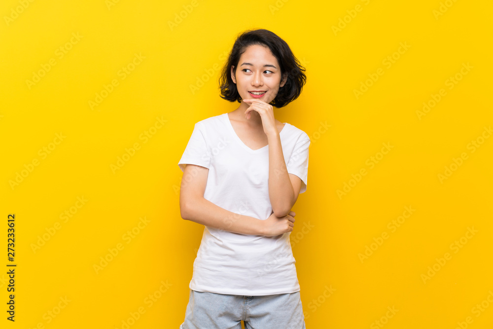 Asian young woman over isolated yellow wall looking to the side Asian young woman over isolated yellow wall looking to the side