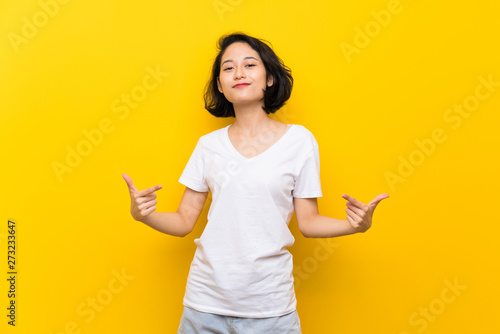 Asian young woman over isolated yellow wall proud and self-satisfied