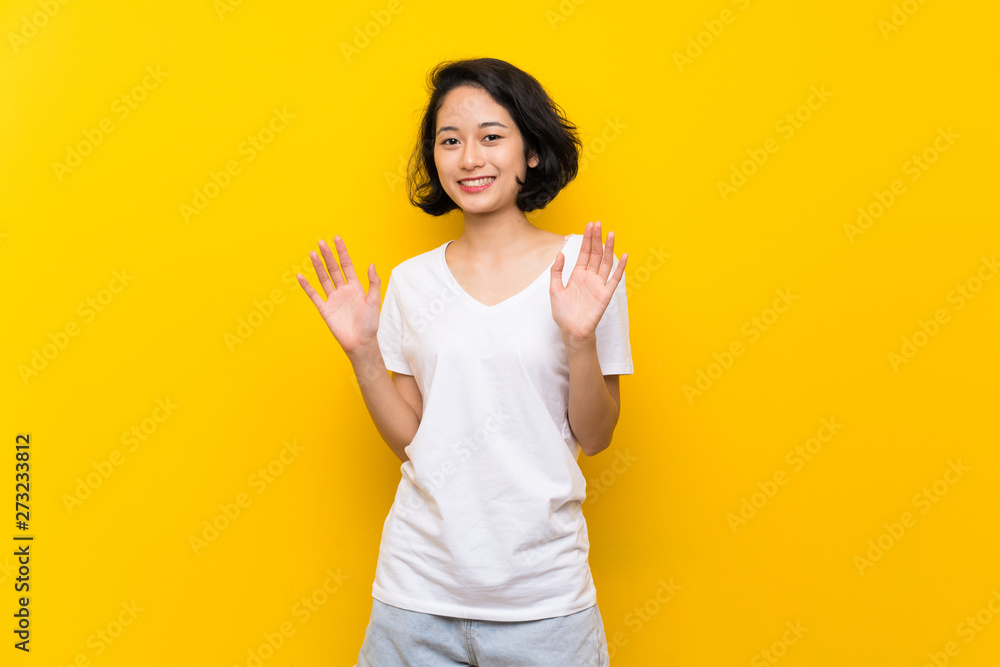 Asian young woman over isolated yellow wall smiling Asian young woman over isolated yellow wall smiling