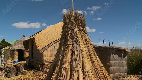 Close-up low angle tilting shot of a stack of dry totora reeds close to a traditional uros reed hut on a floating island, Lake Titicaca, Peru