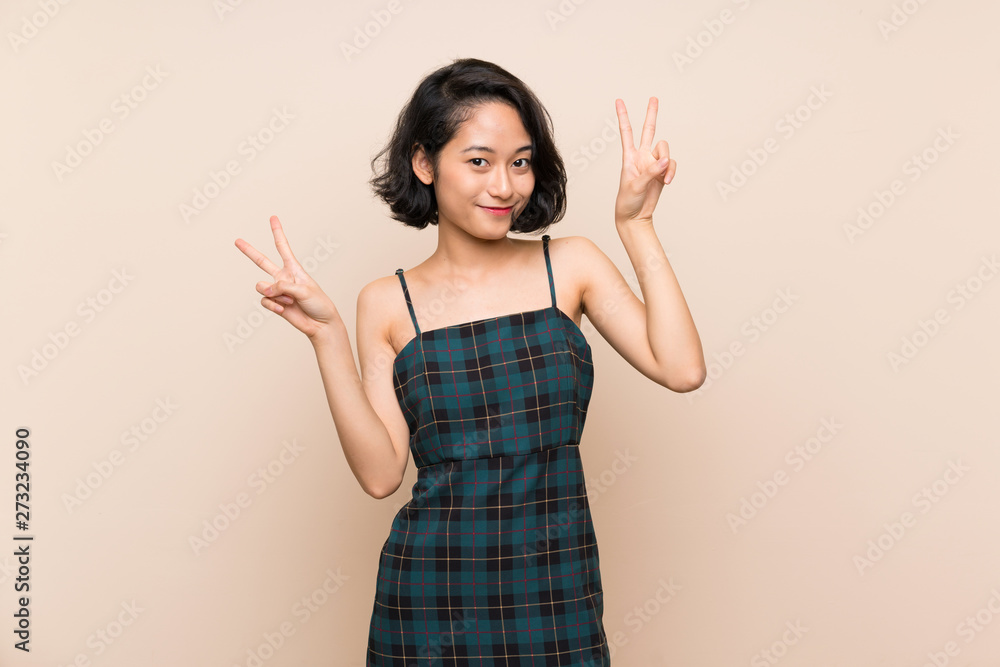 Asian young woman over isolated yellow wall showing victory sign with both hands Asian young woman over isolated yellow wall showing victory sign with both hands
