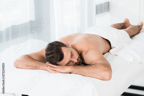 selective focus of handsome bearded man lying on massage table in spa center
