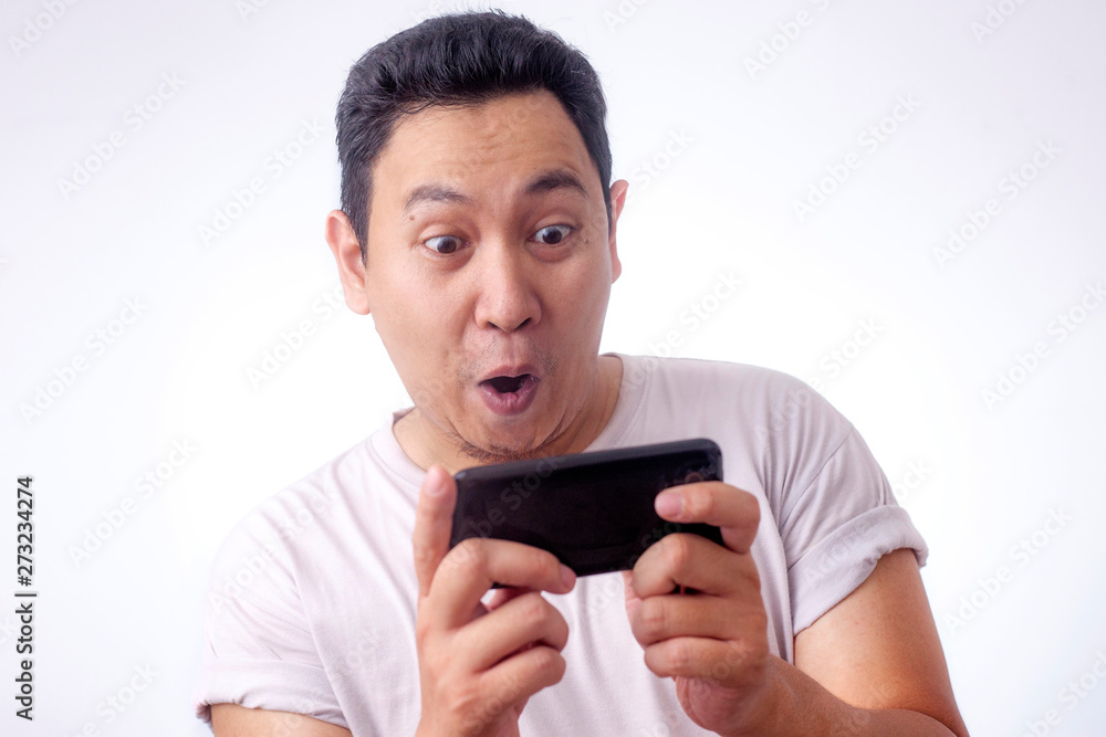 Funny Young Asian Guy Playing Games on Tablet Smart Phone Funny Young Asian Guy Playing Games on Tablet Smart Phone