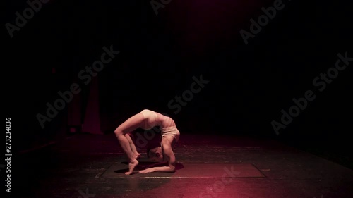 Female contortionist circus performer performing routine in dark studio