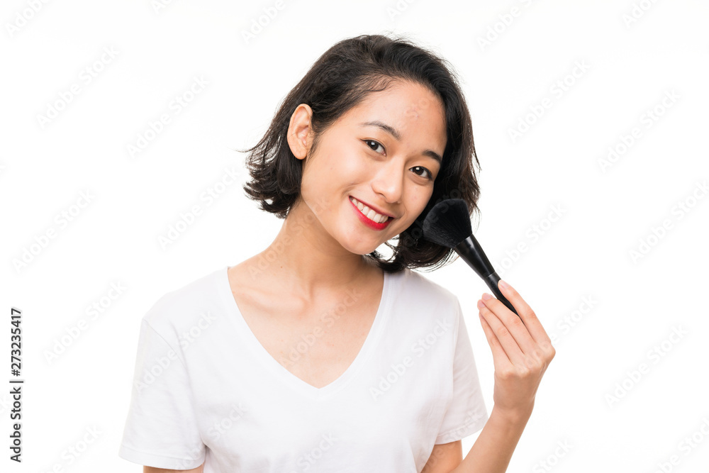 Asian young woman over isolated background with makeup brush Asian young woman over isolated background with makeup brush