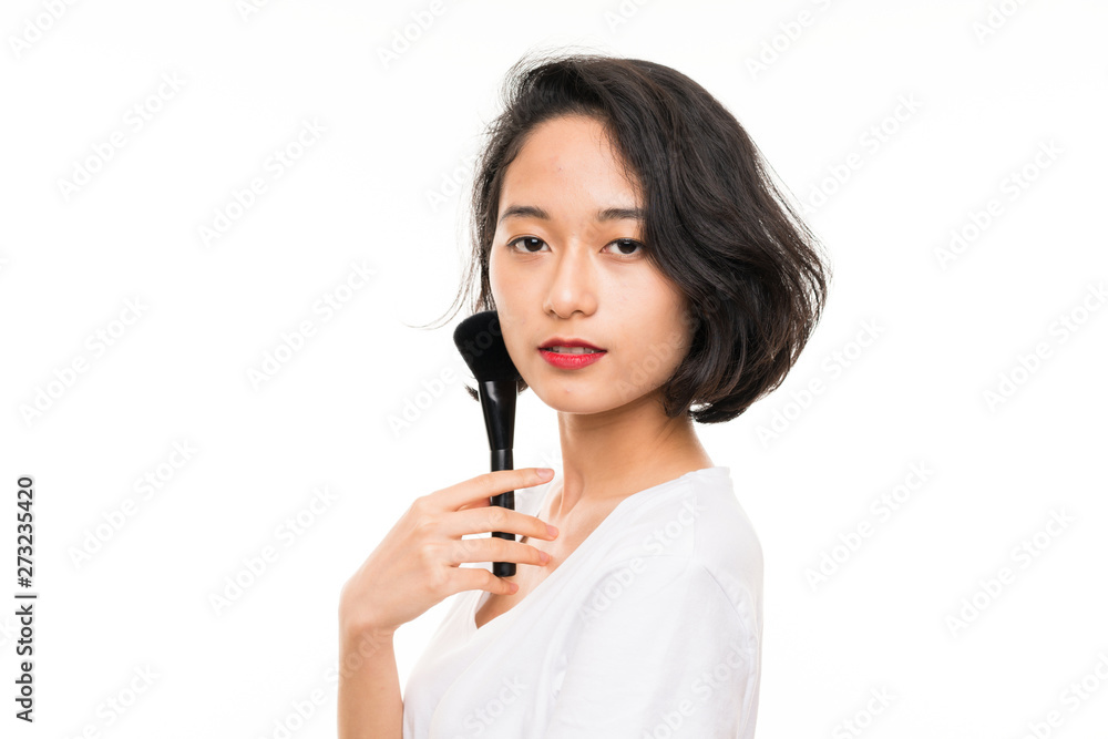 Asian young woman over isolated background with makeup brush Asian young woman over isolated background with makeup brush
