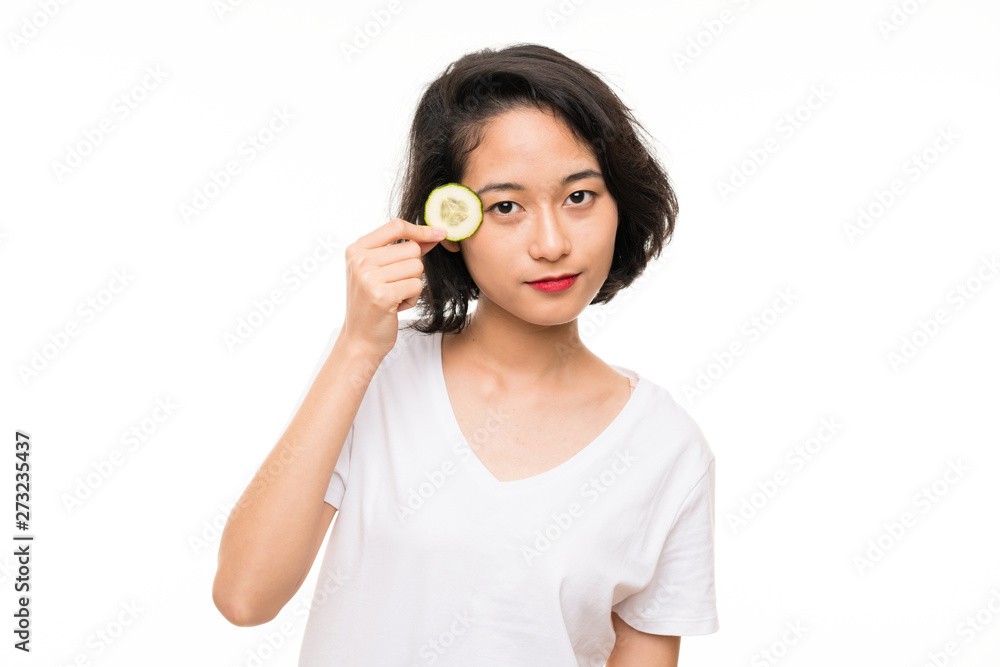 Asian young woman over isolated background holding slices of cucumber Asian young woman over isolated background holding slices of cucumber